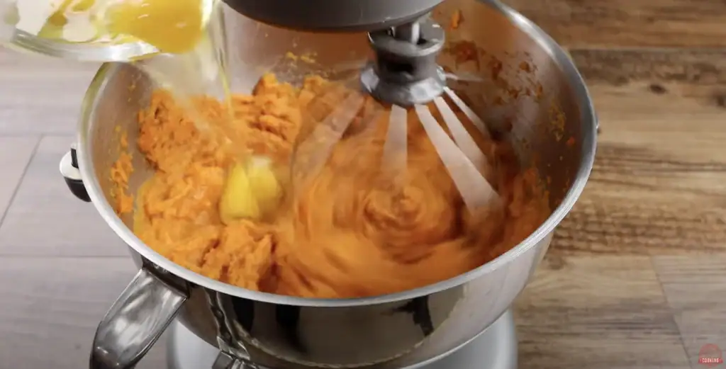 Adding the eggs to the mixing bowl for sweet potato pie
