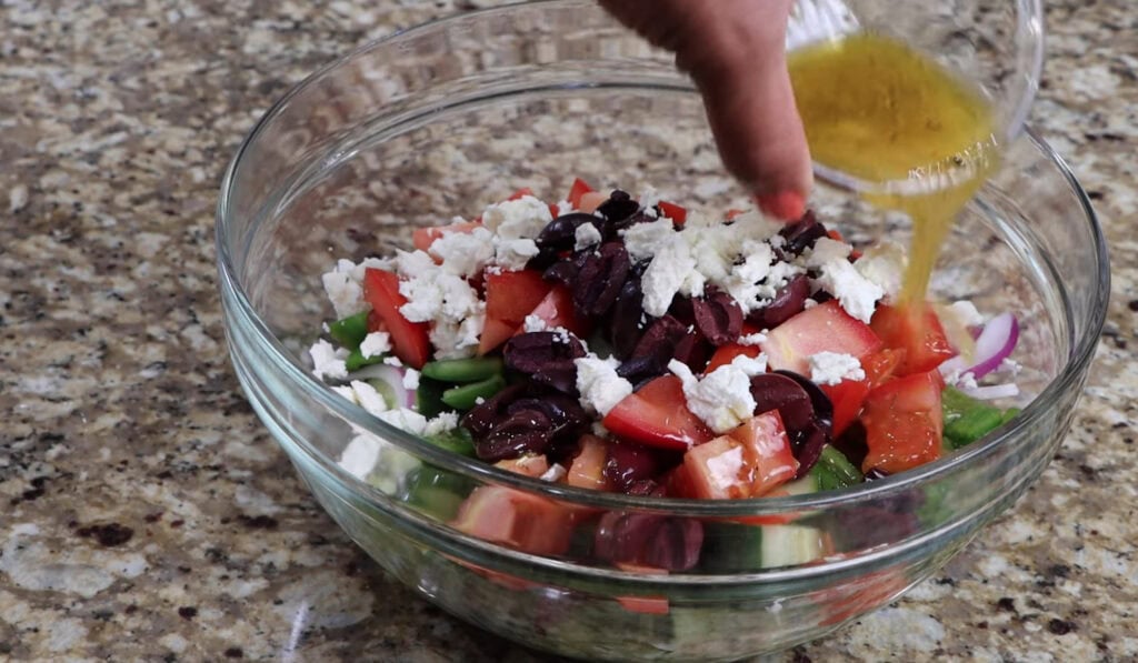Pouring Vinaigrette over Greek Salad in a glass bowl