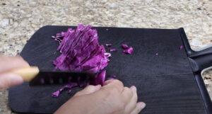 Chopping fresh purple cabbage on a cutting board for homemade shrimp tacos — adds crunch and color to every bite.