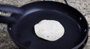 Warming corn tortillas in a skillet until soft and lightly toasted, ready to fill with seasoned shrimp.