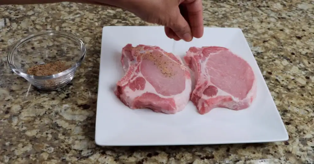 Raw Pork Chops on a white plate being Seasoned