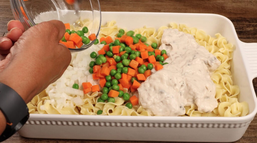 baking dish with egg noodles, cream of mushroom soup, peas and carrots, and onion