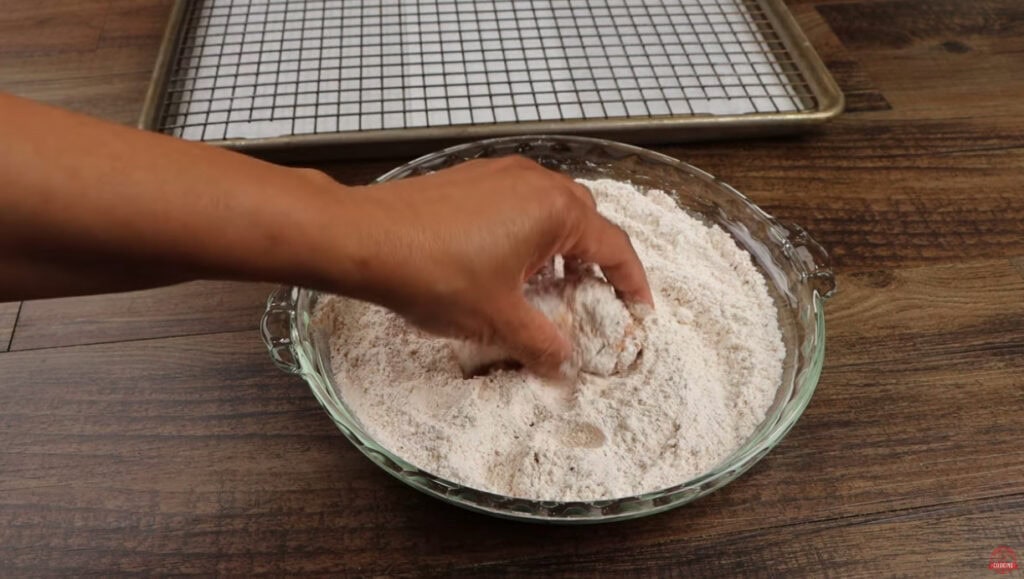 Chicken wing being pressed by hand into a glass dish of seasoned flour for Ghost Pepper Wings
