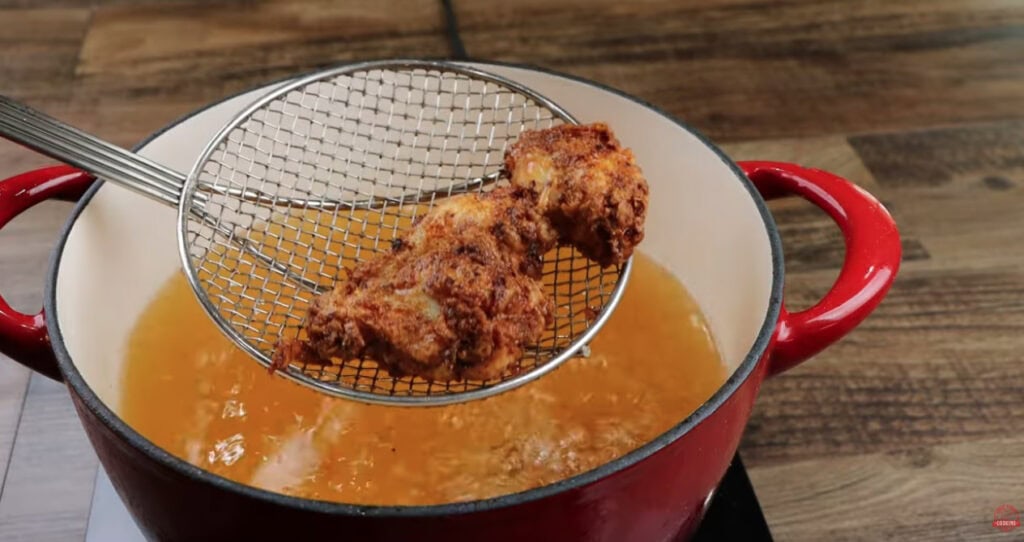Golden fried Ghost Pepper Wing being lifted from hot oil with a spider strainer
