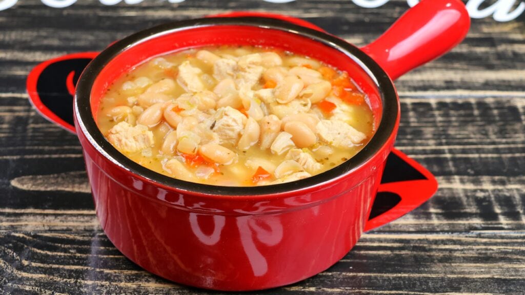 White chicken chili with white beans and red bell pepper served in a red bowl.