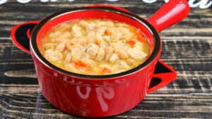 White chicken chili with white beans and red bell pepper served in a red bowl.
