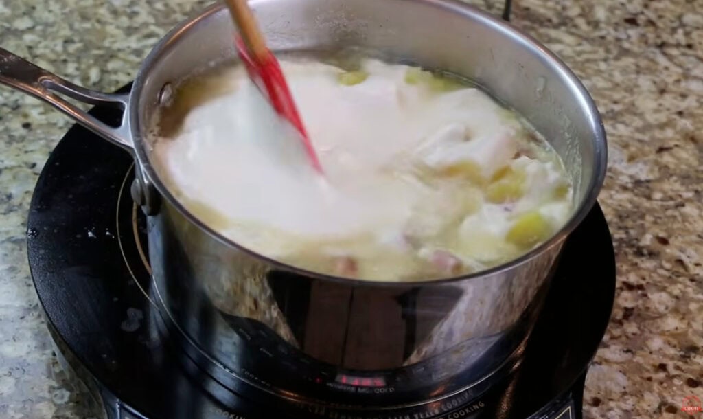 Creamy base being stirred into the ham and potato soup with a red spatula.