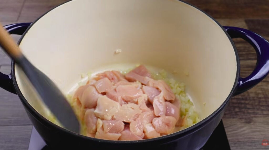 Diced raw chicken added to onion and garlic in a Dutch oven for white chicken chili.