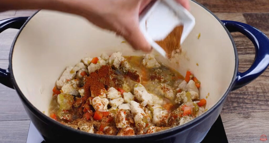Spices being added to chicken and vegetables for white chicken chili.