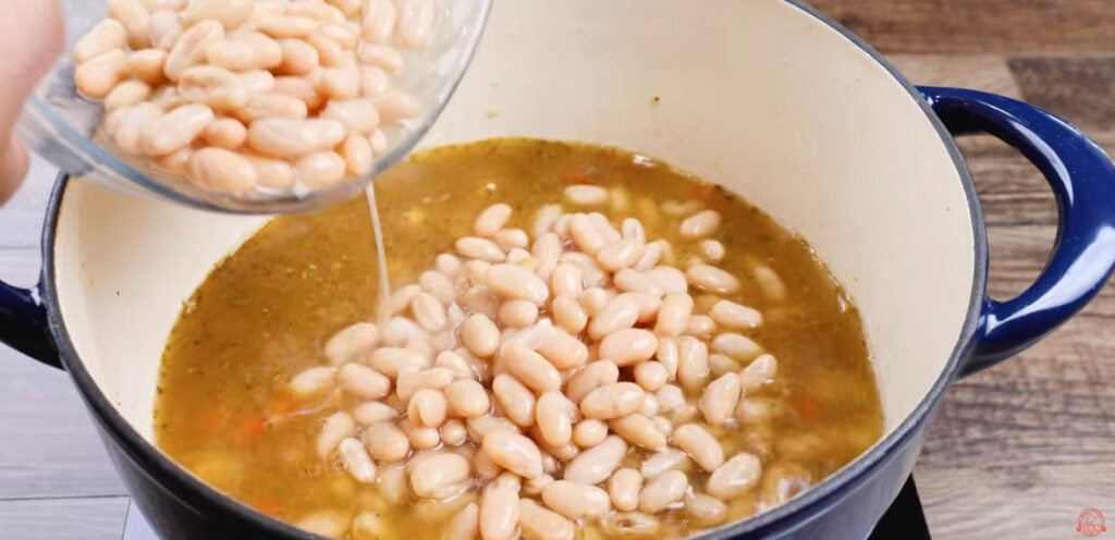 White beans and their liquid being poured into chicken chili in a Dutch oven.