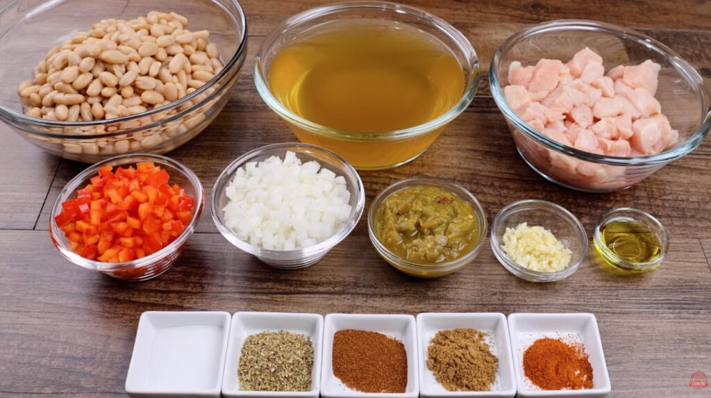 Ingredients for white chicken chili arranged in bowls, including chicken, white beans, broth, bell pepper, onion, garlic, and spices.
