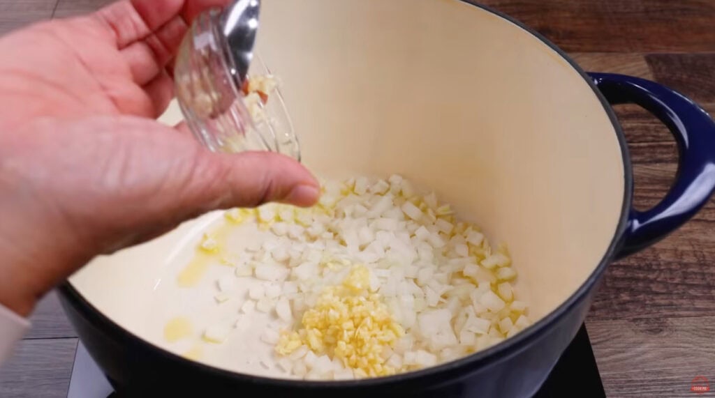 Minced garlic being added to diced onion and olive oil in a Dutch oven.